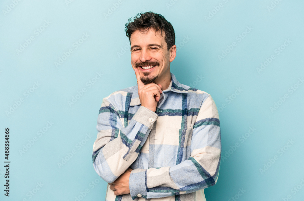 Fototapeta premium Young caucasian man isolated on blue background smiling happy and confident, touching chin with hand.