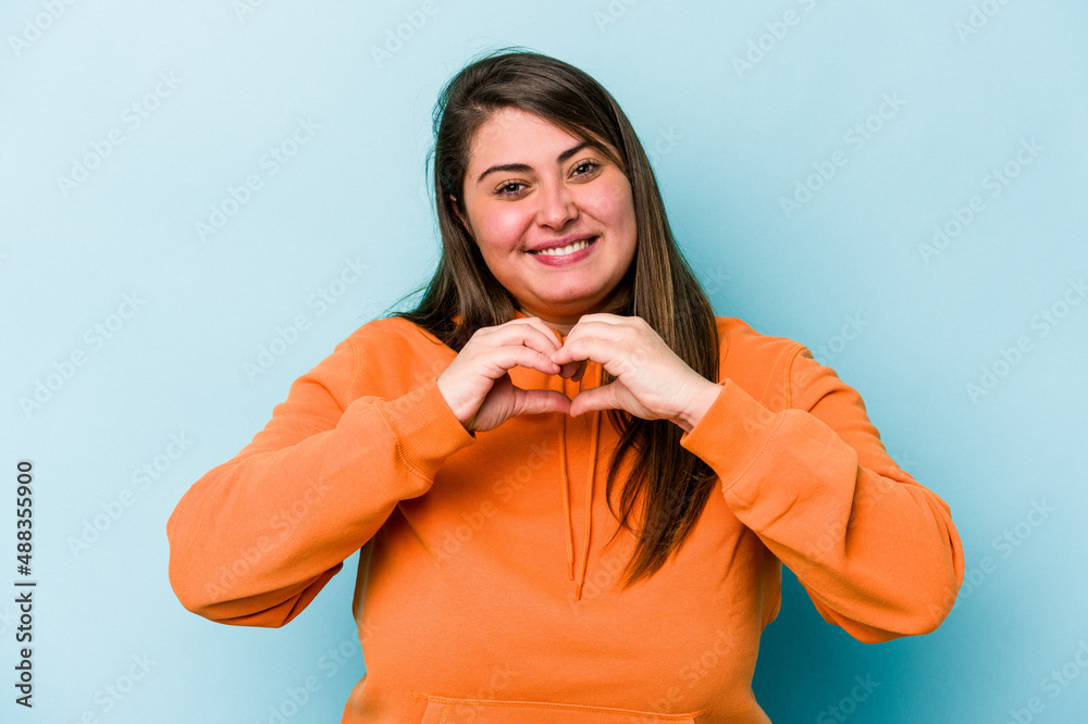 Young caucasian overweight woman isolated on blue background smiling and showing a heart shape with hands. Young caucasian overweight woman isolated on blue background smiling and showing a heart shape with hands.