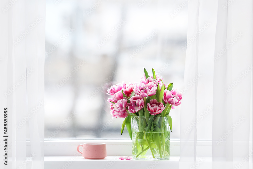 Vase with beautiful tulips and cup on windowsill in room