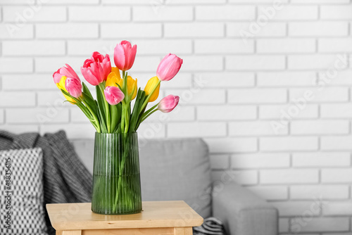 Vase with tulips on wooden stool near sofa