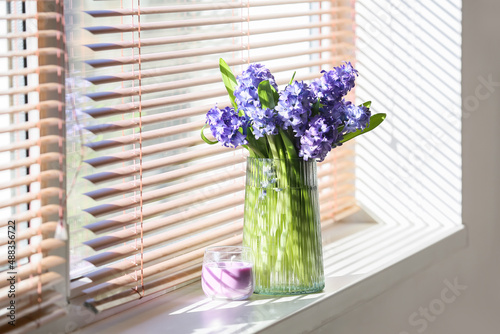 Glass vase with beautiful hyacinth flowers and candle on windowsill