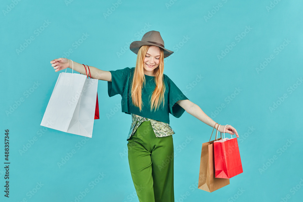 Happy young woman holding shopping bags staying. Pretty girl walk shopping center carry many packs good on blue background. Happy young woman holding shopping bags staying. Pretty girl walk shopping center carry many packs good on blue background.