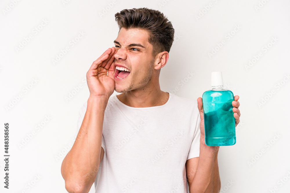 Young caucasian man holding mouthwash isolated on white background shouting and holding palm near opened mouth. Young caucasian man holding mouthwash isolated on white background shouting and holding palm near opened mouth.