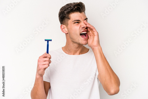 Young caucasian man shaving his beard isolated on white background shouting and holding palm near opened mouth.