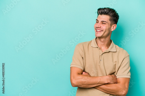 Young caucasian man isolated on blue background smiling confident with crossed arms.