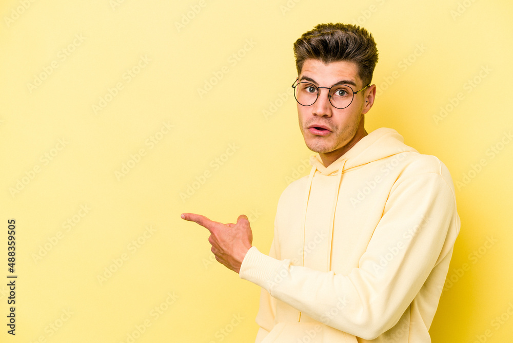 Young caucasian man isolated on yellow background smiling and pointing aside, showing something at blank space. Young caucasian man isolated on yellow background smiling and pointing aside, showing something at blank space.