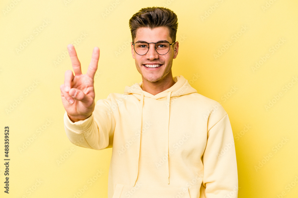 Young caucasian man isolated on yellow background showing victory sign and smiling broadly.