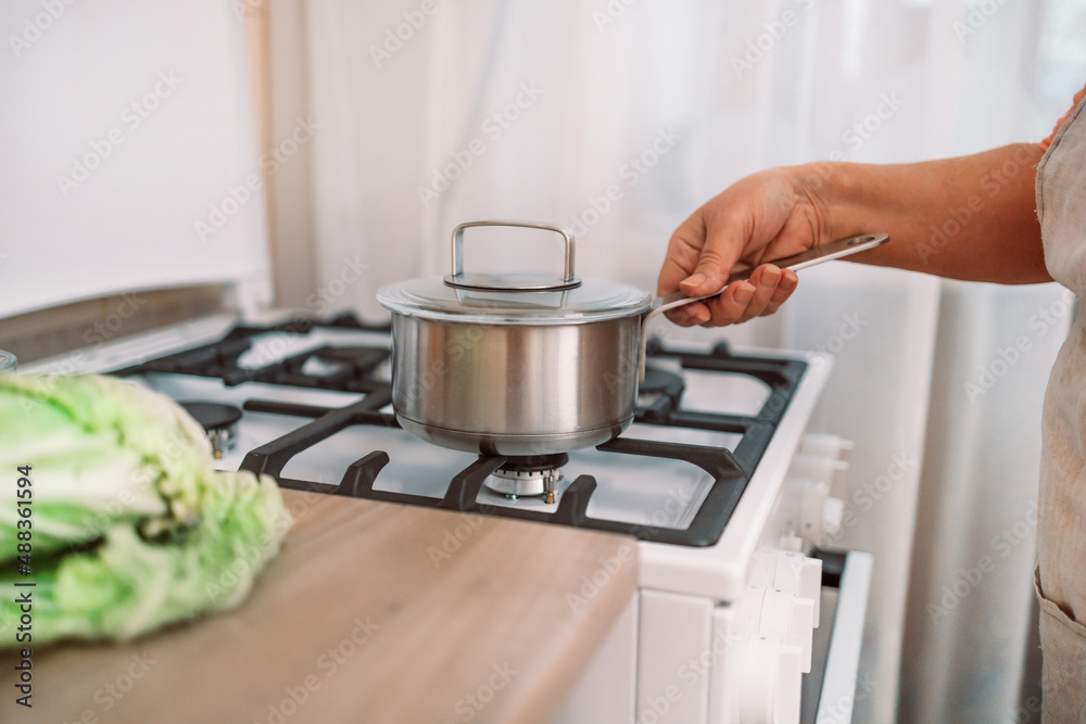 Woman puts stainless steel pot on gas stove in modern kitchen. Cooking utensils concept Woman puts stainless steel pot on gas stove in modern kitchen. Cooking utensils concept