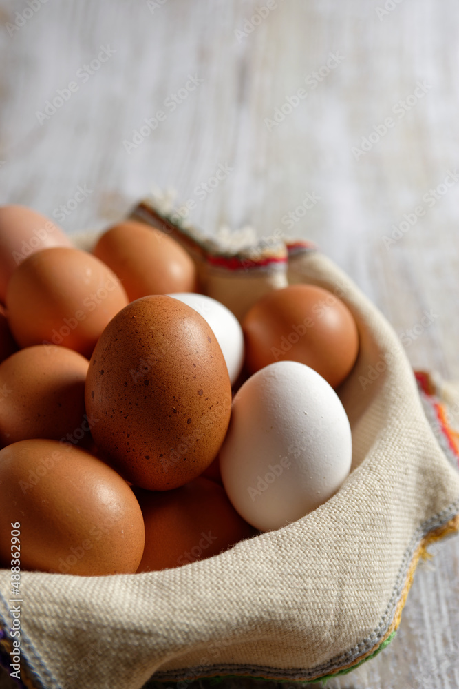 Close-up view of brown and white chicken eggs, in a wicker basket on gray wood. Vertical view. Close-up view of brown and white chicken eggs, in a wicker basket on gray wood. Vertical view.