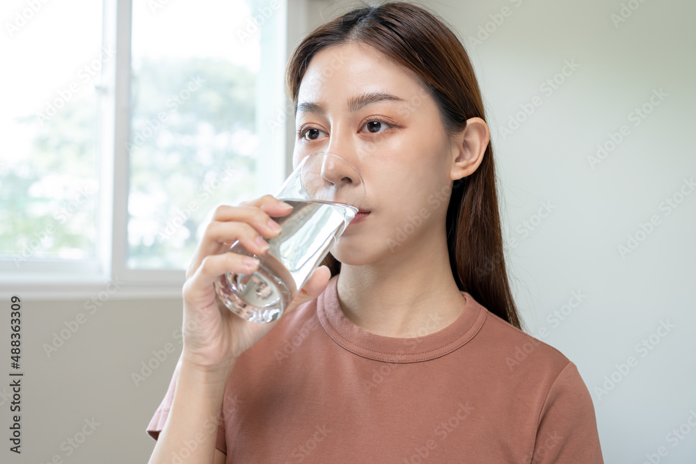 Happy beautiful, asian young woman, girl drinking, sip fresh glass of water for hydration of body, holding transparent glass in her hand, thirsty at home. Health care, healthy lifestyle concept. Happy beautiful, asian young woman, girl drinking, sip fresh glass of water for hydration of body, holding transparent glass in her hand, thirsty at home. Health care, healthy lifestyle concept.