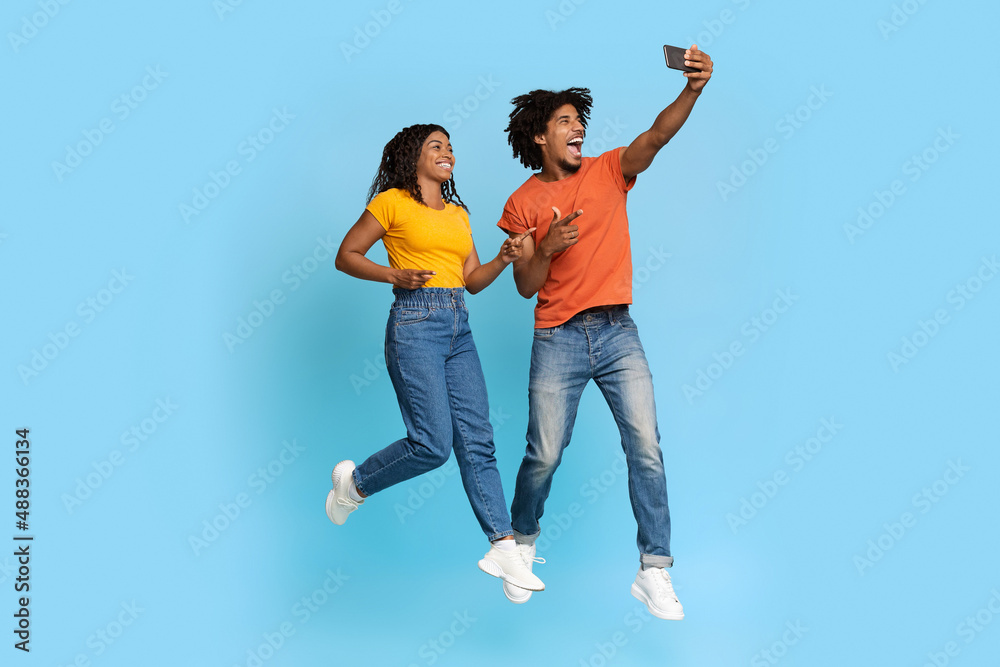Cheerful african american lovers taking selfie together on blue Cheerful african american lovers taking selfie together on blue