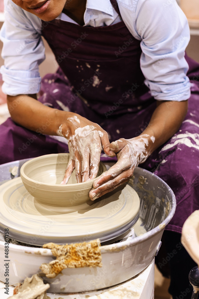 Woman ceramic artist molding clay on pottery wheel at art workshop. Mid section view.