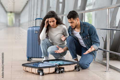 Missed Items. Confused young arab couple sitting near open suitcase in airport