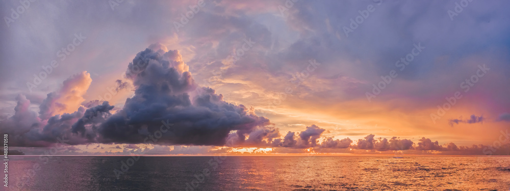 Fototapeta premium a beautiful large purple cloud floats across the colorful sky over the quiet sea. an unusually beautiful evening sunset landscape from the shore of a tropical island