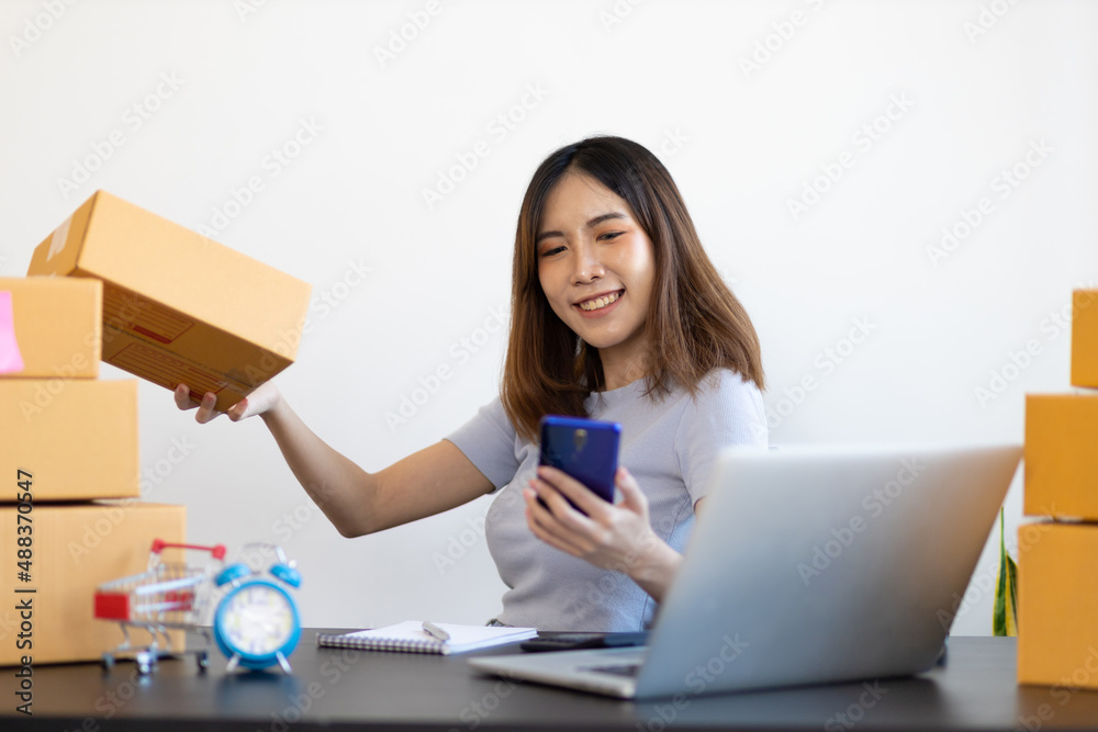 Young Asian woman starting a small e-commerce business working on laptop internet and talking to customers over the phone. Young Asian woman starting a small e-commerce business working on laptop internet and talking to customers over the phone.