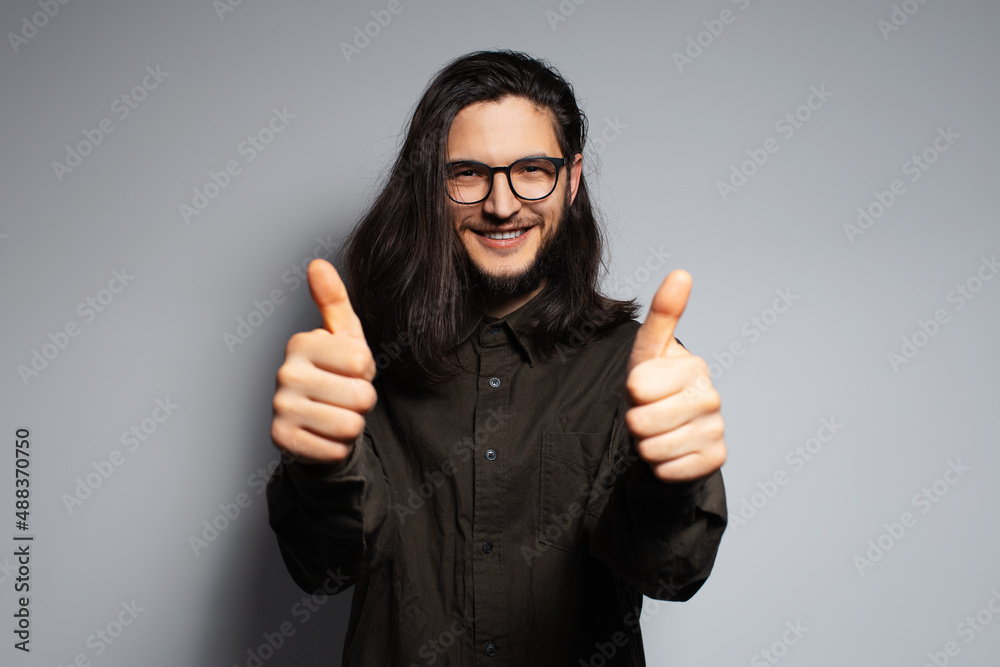 Portrait of young confident attractive man with long hair, gesturing thumbs up. Portrait of young confident attractive man with long hair, gesturing thumbs up.