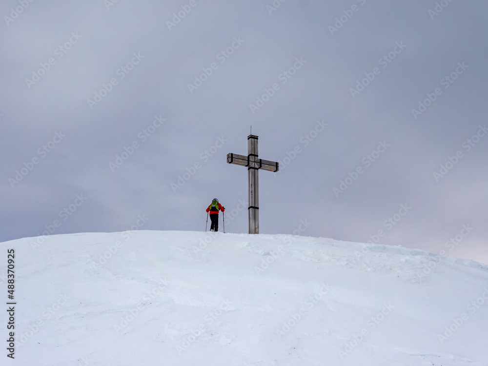 Bergsteiger auf einem Gipfelkreuz in den Alpen Bergsteiger auf einem Gipfelkreuz in den Alpen