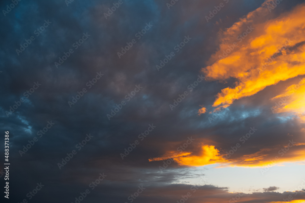 Colourful sunlight of sunset falls on dark cloudy sky. Natural landscape.