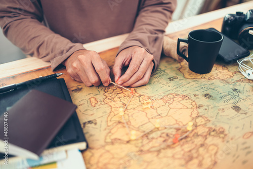 Tourist planning vacation, holiday with the help world map. Man's hand marks route on map and using pins and rope.