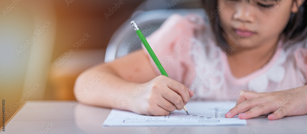 Close up of kid student holding a pencil writing on answer sheet paper Close up of kid student holding a pencil writing on answer sheet paper