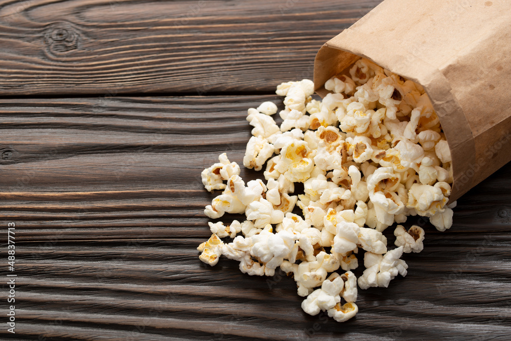 Popped corn snack in paper bag on wooden table closeup