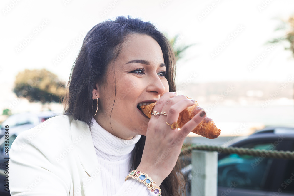 Young caucasian woman eating a croissant on a terrace next to the beach. Young caucasian woman eating a croissant on a terrace next to the beach.