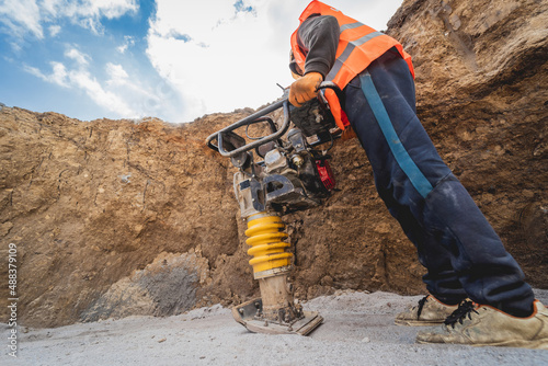 Worker uses a portable vibration rammer at construction of a power transmission substation