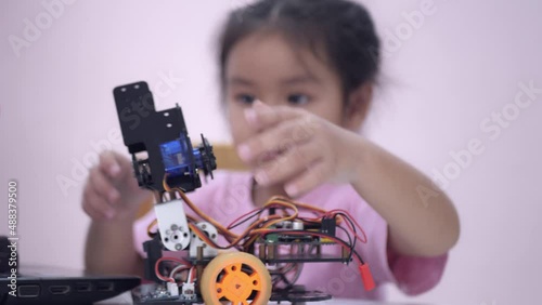 Slow motion scene of Asian girls in glasses holding a robot. A girls in a pink shirt and glasses sits at a table in front of him having a robot made by a girls. He is very satisfied with his work.