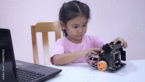 Slow motion scene of Asian girls in glasses holding a robot. A girls in a pink shirt and glasses sits at a table in front of him having a robot made by a girls. He is very satisfied with his work.