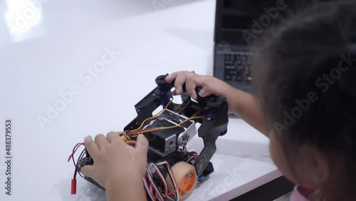 Slow motion scene of Asian girls in glasses holding a robot. A girls in a pink shirt and glasses sits at a table in front of him having a robot made by a girls. He is very satisfied with his work.
