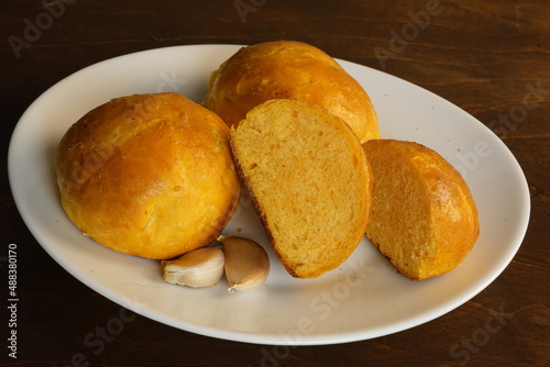 Pumpkin buns and garlic cloves in a white plate on a wooden table.
