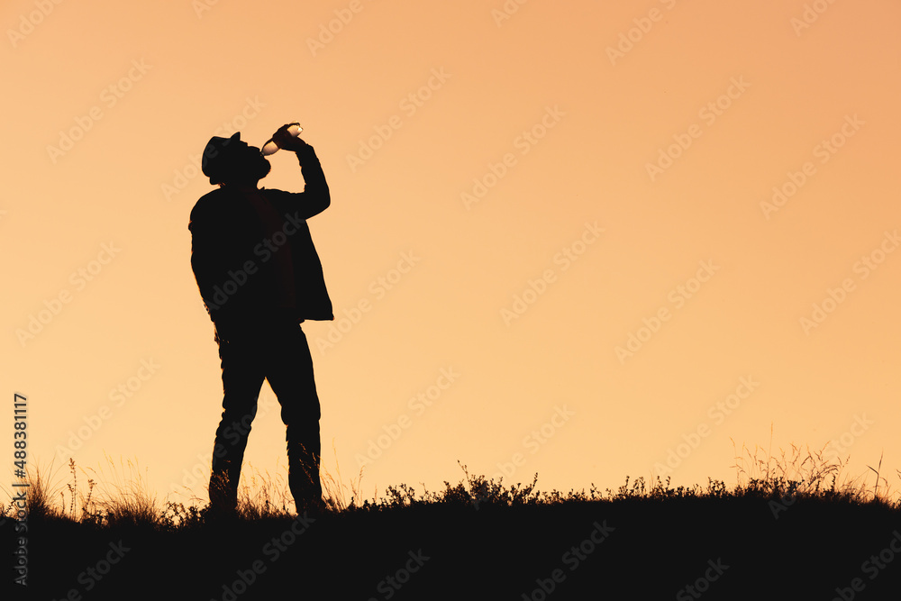 silhouette of a man in a hat who drinks water from a bottle