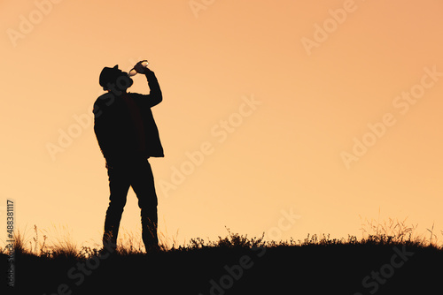 silhouette of a man in a hat who drinks water from a bottle