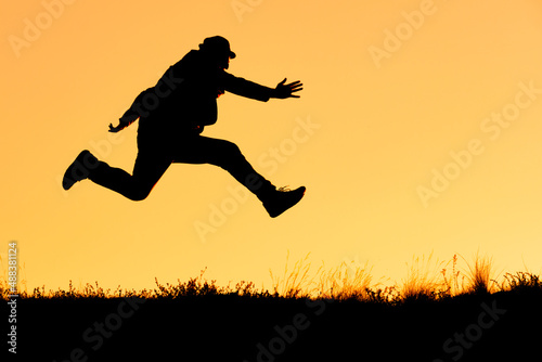 silhouette of a man in a hat while running and jumping on an orange background