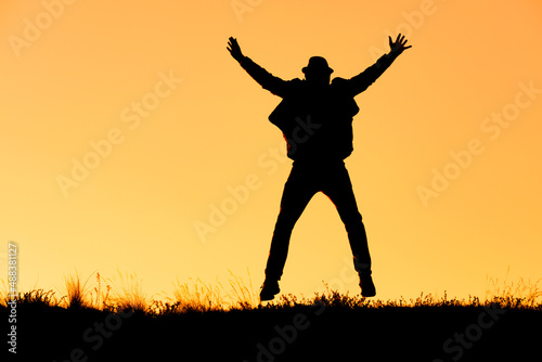 silhouette of a man jumping for joy in a hat, arms and legs in different directions