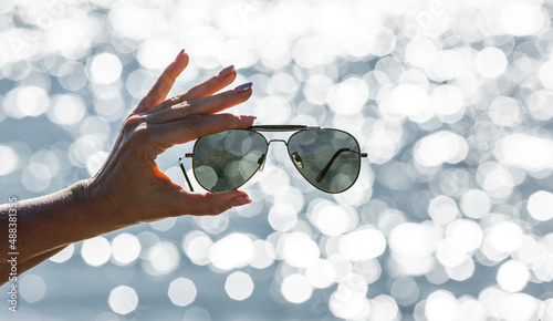 Sonnenbrille in einer Frauenhand vor unscharfen Hintergrund mit Bokeh Reflexen