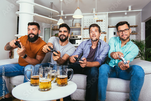 Smiling male friends with gamepads and beer playing video game at home