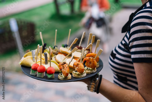Fototapeta Naklejka Na Ścianę i Meble -  Waitress in holding a plate with canapes. Catering service. Wedding welcome food..Сanapes (shrimp, mozzarella, sun-dried tomatoes). Welcome buffet at the event.