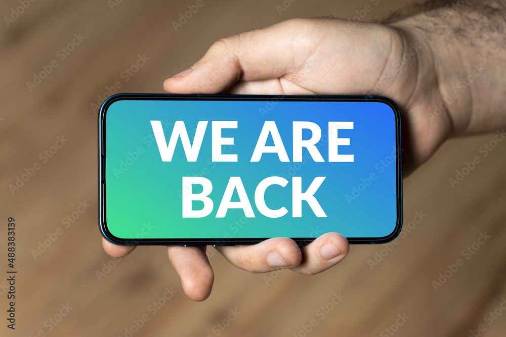 We are back - hand holding a phone We are back - hand holding a phone