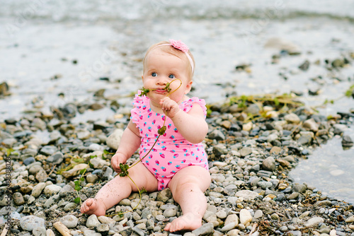 Outdoor portrait of adorable baby girl playing with seaweed by the river, wearing pink swimsuit © annanahabed