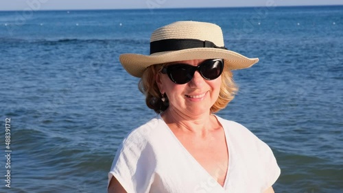 beautiful 50 year old woman in a straw hat and sunglasses on a blue sea background. Summer, vacation, vacation, active retirees