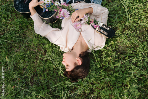 Young woman lying on the grass holding guitar covered with flowers outdoor