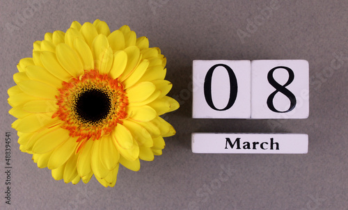 Wooden calendar with the date "March 8" on a gray background with a yellow gerbera flower. International women's day, congratulations to women. March 8