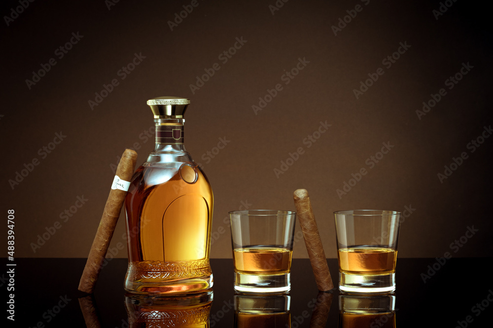 close up view of cigars, bottle of whiskey and two glasses aside on color back. close up view of cigars, bottle of whiskey and two glasses aside on color back.