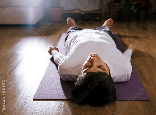 Man is lying on floor on yoga mat in shavasana pose. Concept of yoga and relaxation. photo