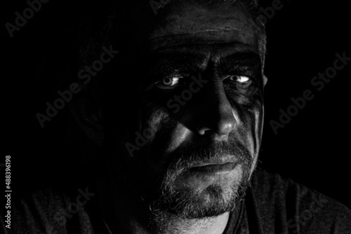 Viking man with a furious gaze and a painted face looks into the darkness with bright eyes