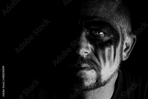Viking man with a furious gaze and a painted face looks into the darkness with bright eyes