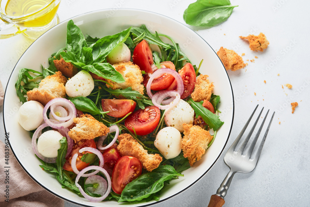 Panzanella Bread Salad. Traditional food of Italy with tomatoes, mozzarella balls, basil, onion and bread on light grey background. Traditional Italian cooking. Top view. Copy space.