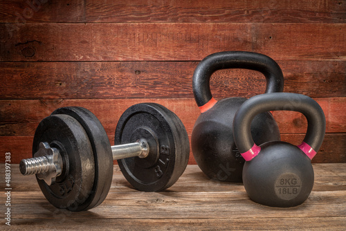 cast iron dumbbell and kettlebells on a grunge wooden deck - fitness concept