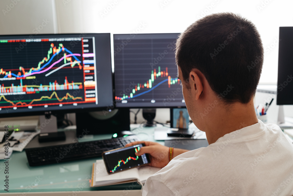 Successful young trader in casual wear working with charts and market reports at home